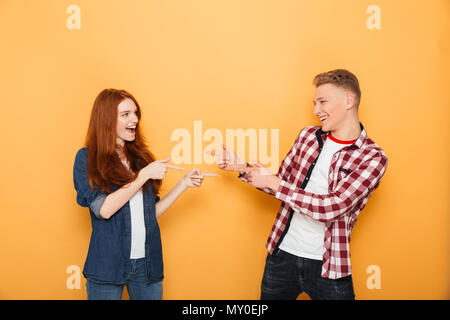 Portrait of a happy teenage couple pointing fingers at each other isolated over yellow background Stock Photo