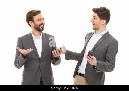 Portrait of a two satisfied business men holding mobile phones and talking isolated over white background Stock Photo