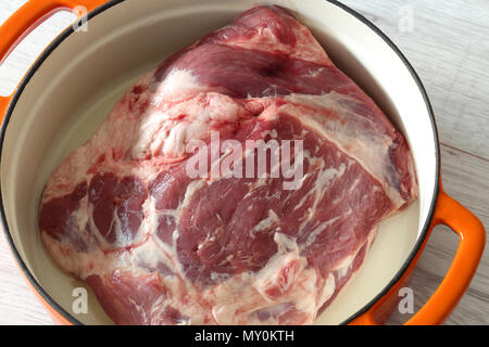 Raw shoulder of lamb in an orange ceramic roasting dish prepared to be cooked Stock Photo