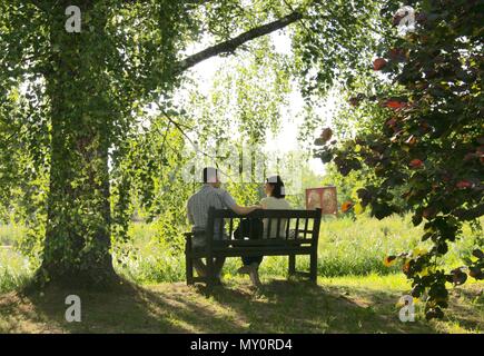 Couple sitting on a bench in a park at sunset in an idyllic atmosphere Stock Photo