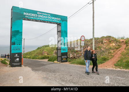 A couple of vacationers posing for pictures in front of Welcome to the Biggest Waves in the World gate at Nazare, Portugal. Stock Photo