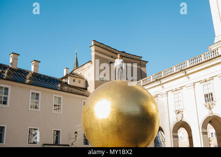 Austria, Salzburg - 01. 01. 2017. View of golden ball statue with man in formal outfit on top placed on city square in sunlight Stock Photo