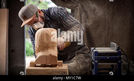 Experienced carpenter in work clothes   saws a man's head with a tree , using an angle grinder  in the workshop, around a lot of tools for work Stock Photo
