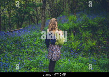 A young mother with a baby is standing in a meadow of bluebells Stock Photo