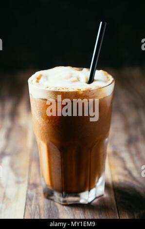 Iced coffe latte with milk foam and a straw on a rustic wooden table Stock Photo