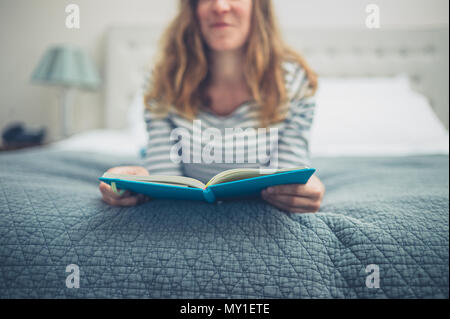 A young woman is lying on a bed and is reading a book Stock Photo