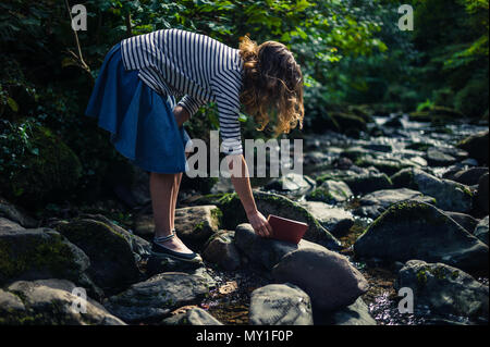 A young woman is discovering and picking up a book in a river Stock Photo