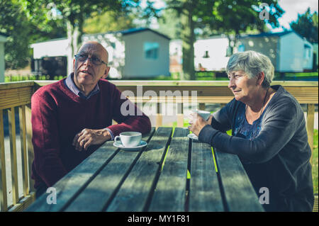 A senior couple are sitting at a table in a caravan park and are drinking coffee Stock Photo