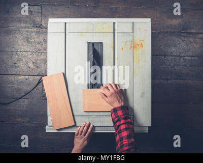 A young man's arm and hand operating a tablesaw Stock Photo