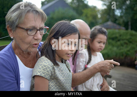 Family portrait of an elderly caucasian couple and their mixed race grandchildren in an unposed natural setting in the back yard in summer sunshine Stock Photo