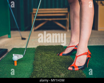 A woman in heels is hitting golf balls on a driving range Stock Photo