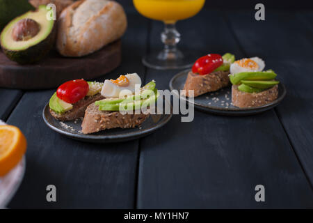 Toasts with avocado, yatsom and cherry tomatoes, on a black wooden background. Healthy and tasty food. Fitness food. Stock Photo