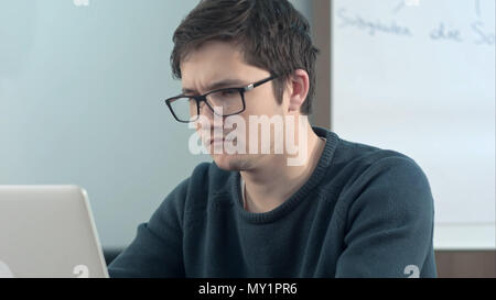 Young pensive student working on laptop at home office or library with serious face Stock Photo