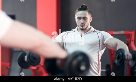 Muscular bodybuilder doing exercises with dumbbells in gym Stock Photo
