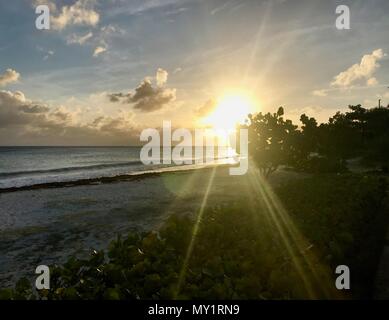 Sunset at a coastal street in Oistins, Barbados (Caribbean Island) with palm trees, beach and beautiful turquoise ocean in the background Stock Photo