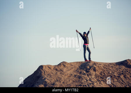 Full-length picture of woman growing tourist with backpack and walking sticks with hands up on mountain Stock Photo