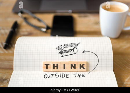 Closeup on notebook over wood table background, focus on wooden blocks with letters making Think Outside the Box text. Stock Photo