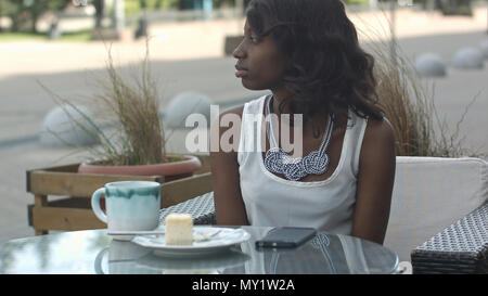 Portrait of african female freelancer at cafeteria looking tired and bored, drinking coffee and using smartphone Stock Photo