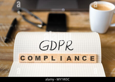 Closeup on notebook over wood table background, focus on wooden blocks with letters making GDPR Compliance text. Stock Photo