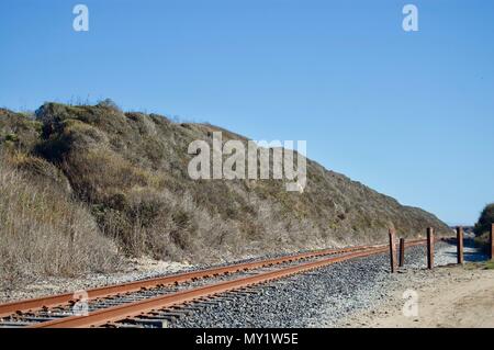 Lonely abandoned railway tracks surrounded by a beautiful coastal view in California (USA) with limestone rock cliffs, greenery & the Pacific ocean Stock Photo