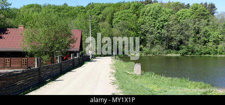 A dirt sandy road leads to the European  no name village along the shore of a clean lake. Spring sunny day panoramic lanscape Stock Photo