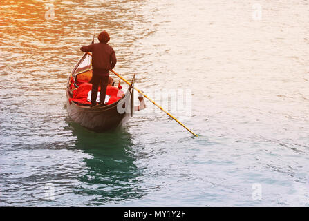 Venetian gondolier punting gondola in a canal waters of Venice Italy with sunshine background. Stock Photo