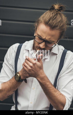 Close-up handsome stylish man in eyeglasses lighting cigarette with lighter Stock Photo