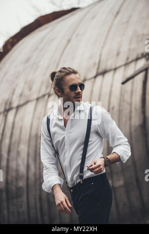 Handsome stylish young man in sunglasses holding cigarette and looking away Stock Photo