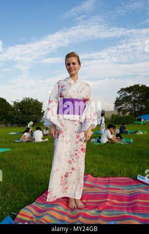 A beautiful blonde European woman wearing a traditional Japanese colorful Yukata with flowers during a summer Matsuri festival celebration in Osaka Stock Photo