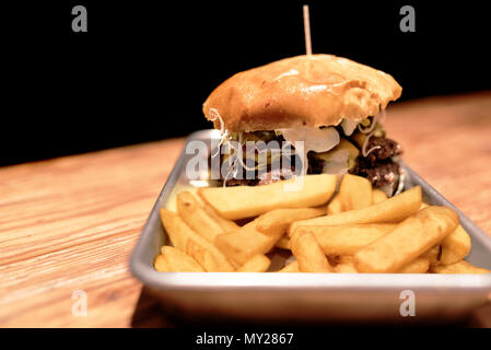 large burger and french fries on metal plate on rustic wooden table against dark background Stock Photo