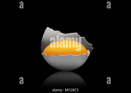 Egg yolk in a cracked white egg shell on isolated black background. Moody close up shoot Stock Photo