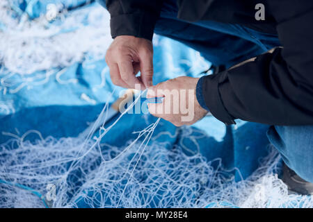 Fisherman mending a fishing net with a net needle on the harbor Stock Photo  - Alamy