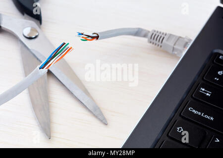 Internet cable connected to a laptop computer cut by a scissors. Concept of internet ban, cencorship and interruption. Stock Photo