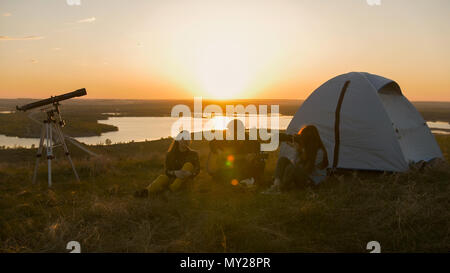 Group of friends sitting on the grass near the tent chilling out at sunset Stock Photo