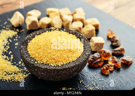 Brown cane sugar in bowl on black slate background closeup Stock Photo
