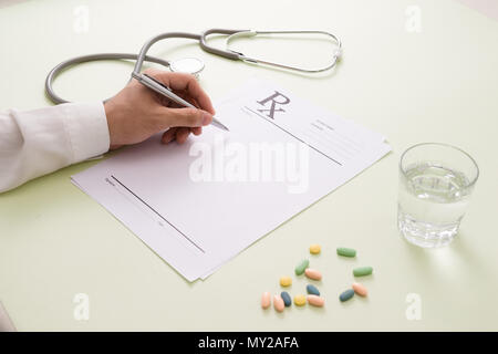 Top view of a doctor's hand writing a prescription. A pill bottle and stethoscope are also on the desk. Stock Photo