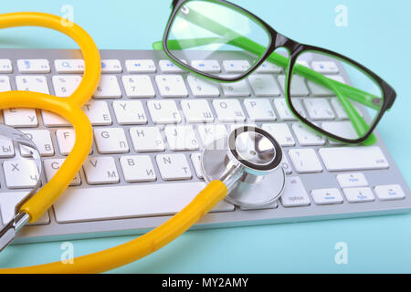 Closeup of a yellow stethoscope lying on notebook keyboard and green glasses. selective focus. Stock Photo
