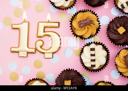Number 15 gold candle with cupcakes against a pastel pink background Stock Photo
