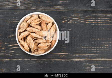 Ceramic bowl filled with Uzbek inshell almonds on wooden background Stock Photo