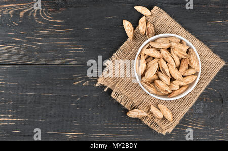 Bowl filled with Uzbek inshell almonds on wooden background, top view Stock Photo