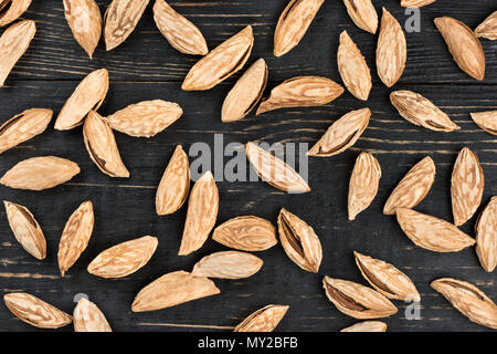 Scattered uzbek inshell almonds on wooden background Stock Photo