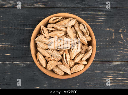 Uzbek inshell almonds in a bowl on wooden background, top view Stock Photo