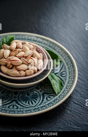Pistachios in shell on blue plate over black slate background Stock Photo