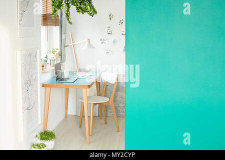 Green empty wall with place for your product in white open space interior with laptop on a wooden desk, fresh plants and handmade posters hanging on t Stock Photo