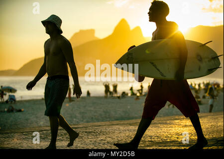 RIO DE JANEIRO - MARCH 20, 2017: Sunset silhouettes of two young surfers with surfboard at Arpoador, Ipanema with two brothers mountain in background Stock Photo