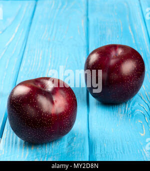 Two large fresh red plums on a blue wooden background Stock Photo