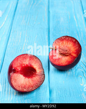 Two halves of juicy red plums on the blue table Stock Photo