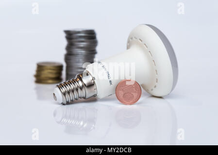 LED economy lamp rests on a white surface next to coins Stock Photo