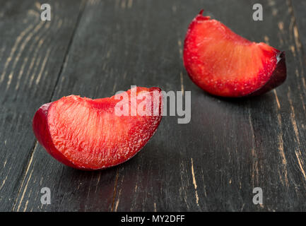 Two juicy slices of red plums on wooden background closeup Stock Photo