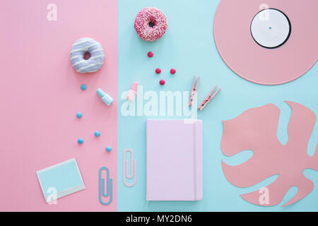 Notebook, nail polishes, clips and donuts on pink and blue background with leaf and vinyl Stock Photo